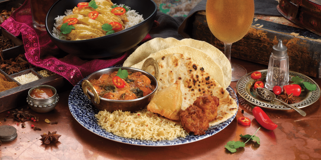 Curry with rice, poppadom, and sides with beer in the background